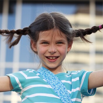 A picture of a child girl in a blue and white striped shirt smiling towards the camera while holding her hair