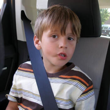 A photo of a boy in a car seat looking at the camera with a striped yellow and brown shirt