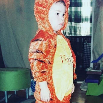 A photo of a toddler looking outside of frame wearing a onsie that looks like a tiger and says 